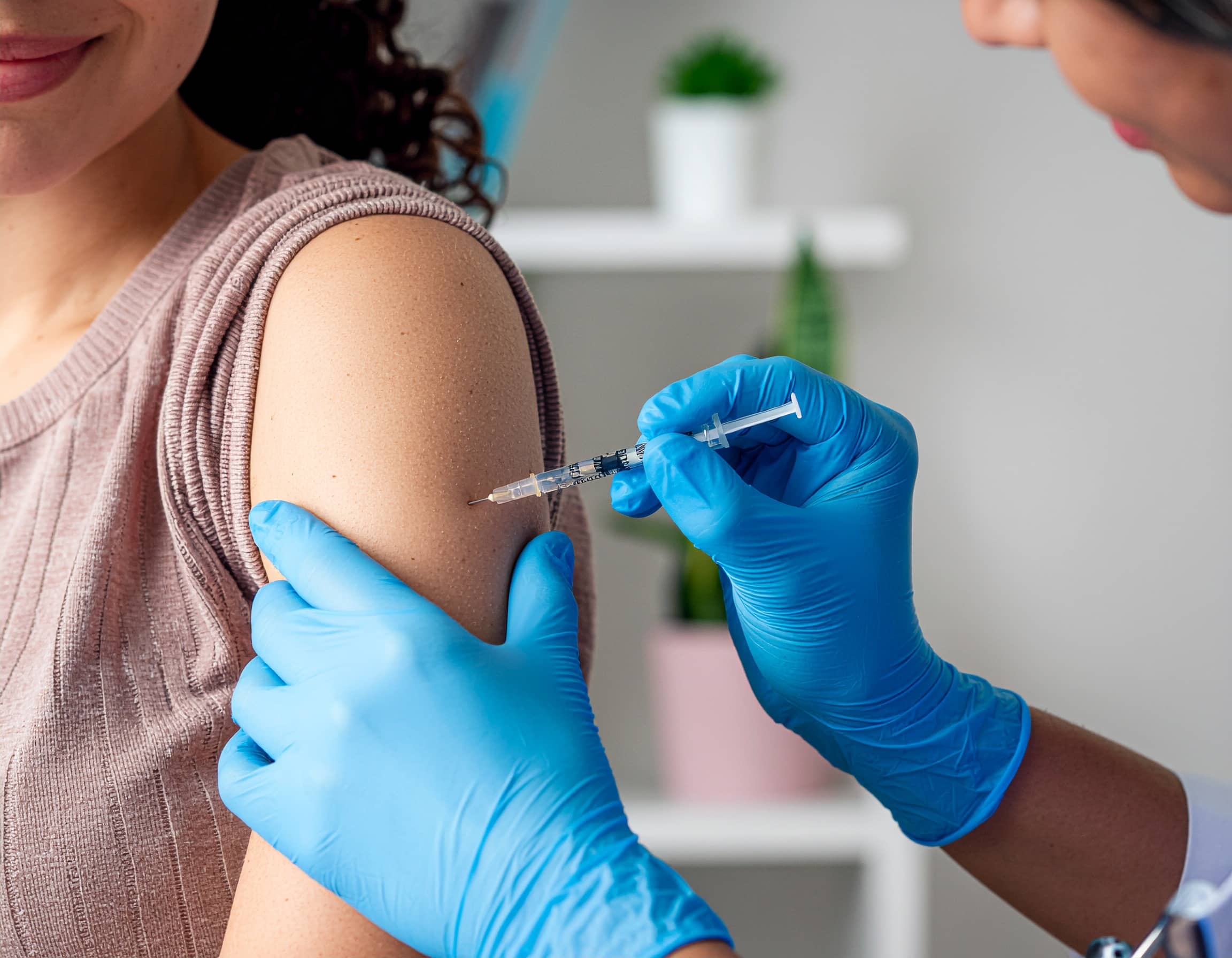 Κορίτσι λαμβάνει εμβόλιο στο χέρι από ιατρικό προσωπικό με γάντια, σε εσωτερικό χώρο.