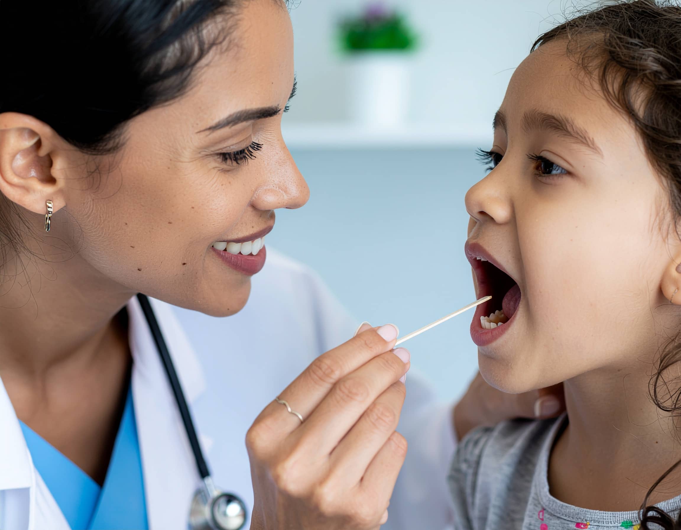 Γιατρός εξετάζει το στόμα μικρού κοριτσιού με ξυλάκι σε παιδιατρικό ιατρείο, σε έλεγχο για λοιμώξεις.