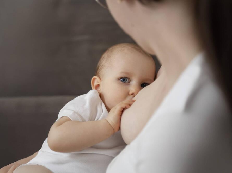 Μητέρα θηλάζει το μωρό της φορώντας λευκή ρόμπα, προβάλλοντας τη στοργή και τη σημασία του μητρικού θηλασμού.